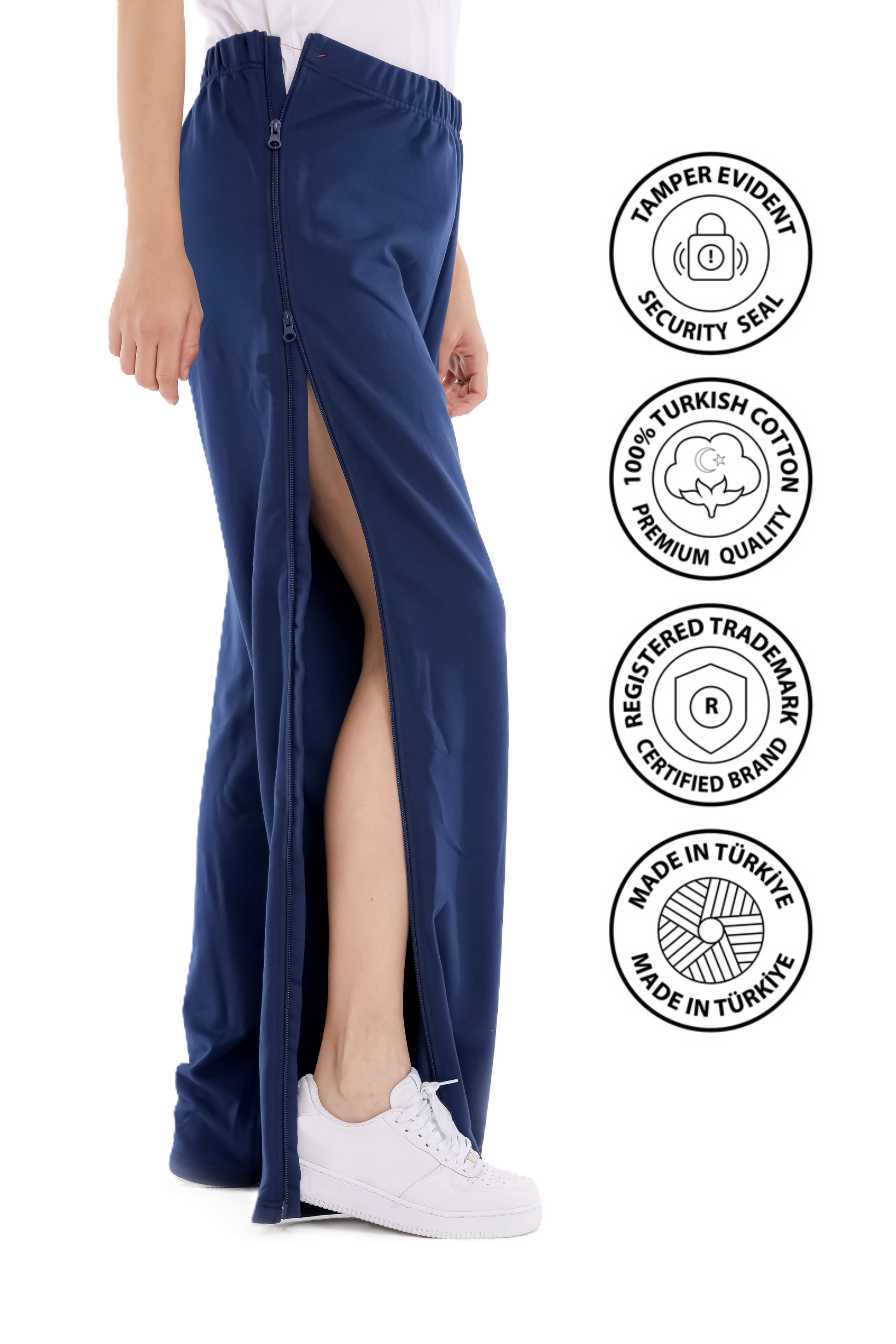 Person wearing blue pants with a high slit, standing against a white background, with brand certification logos displayed. Adaptive_Bedbound_Patient_Care_Trousers_Zip-Open_Inseam_12